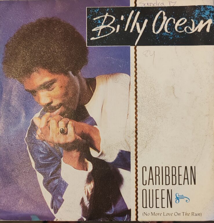 "Pochette vinyle ou CD de la chanson 'Caribbean Queen (No More Love on the Run)' de Billy Ocean, sortie en 1984. On y voit le chanteur souriant, vêtu d'un costume blanc élégant, devant un fond aux couleurs tropicales évoquant les Caraïbes. Illustration typique du style visuel des années 80."
